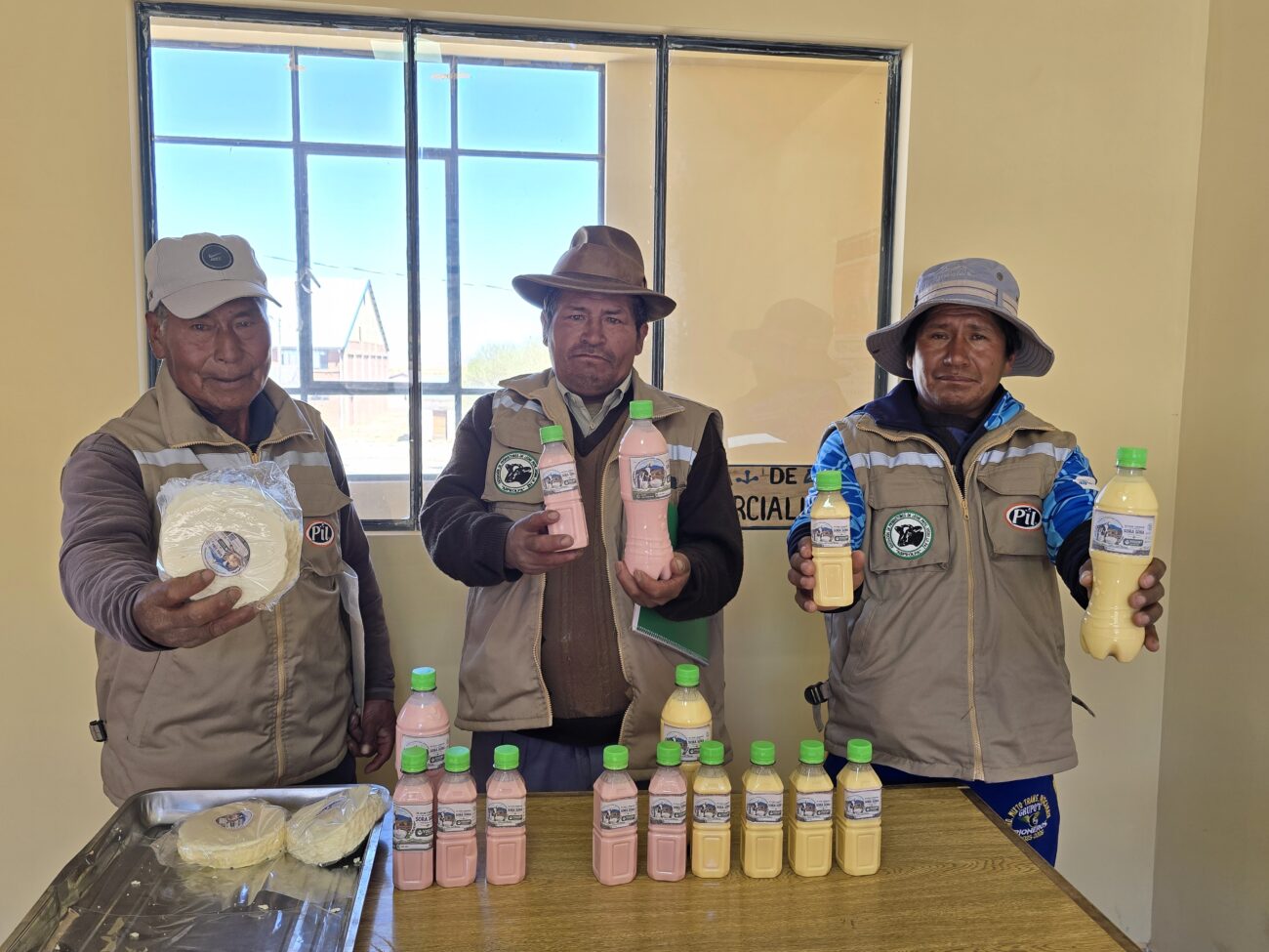  Tres productores de la OECA SORA SORA muestran un queso y botellas con bebidas lácteas de colores rosado y amarillo. Sobre la mesa se observan más quesos y productos embotellados.